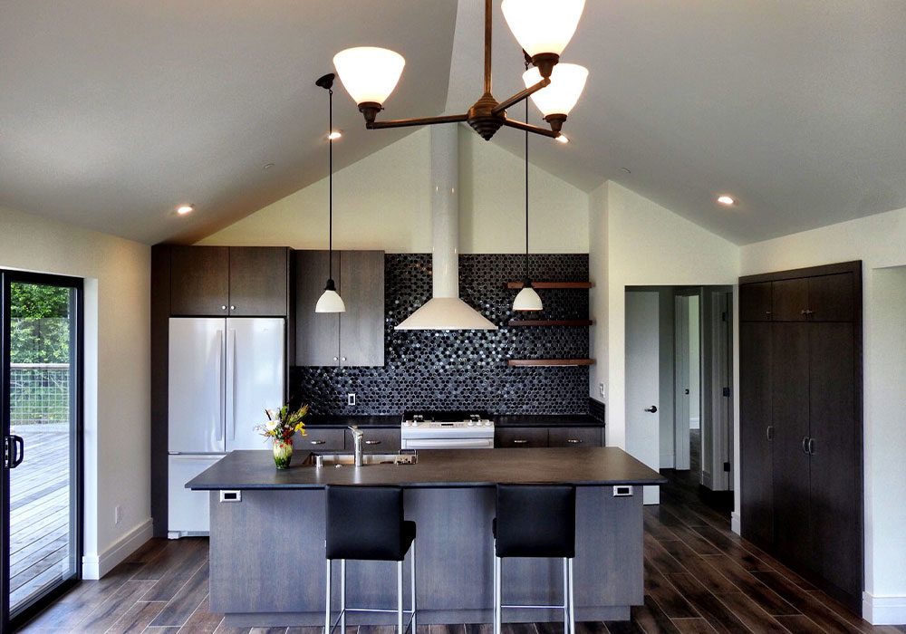 Modern kitchen interior with stainless steel appliances, dark cabinetry, and a central island with seating under pendant lighting.